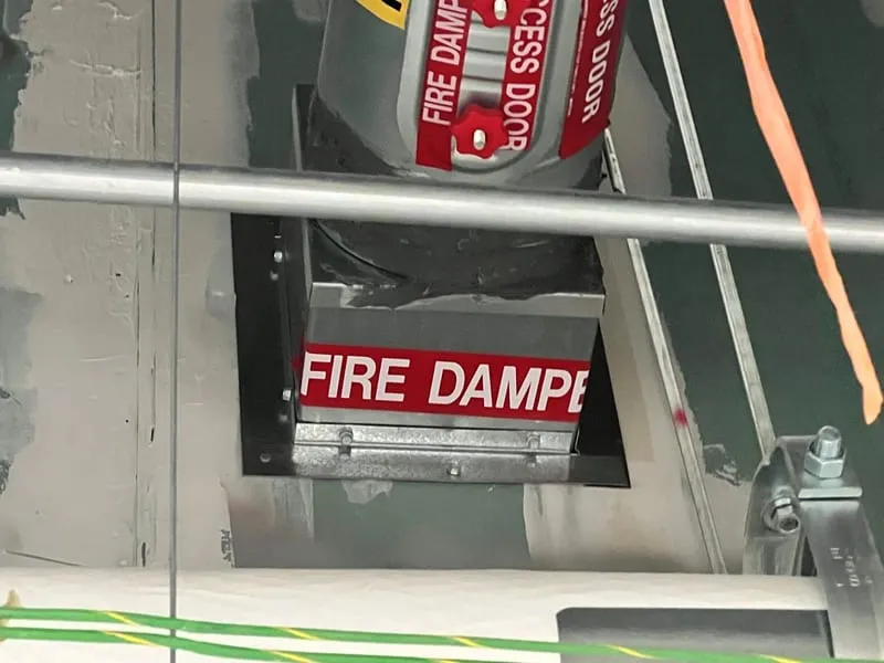 A labelled fire damper with its access door open in a rated assembly.